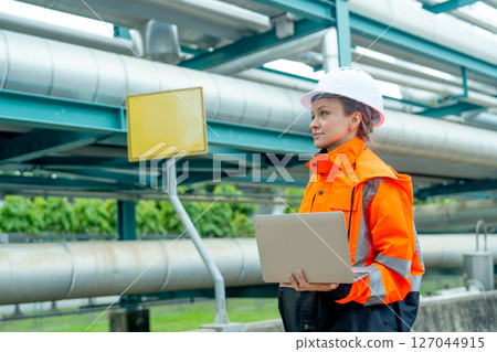 One petrochemical or gas factory worker or technician woman man work using laptop and stand near pipeline in factory workplace. 127044915