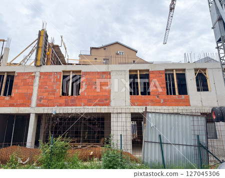 Partially constructed building with exposed red bricks and concrete frame. Urban development scene showing structural elements and ongoing work. 127045306