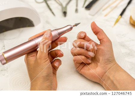 Gel nail manicure at home, female hands with nail drill bit 127046745