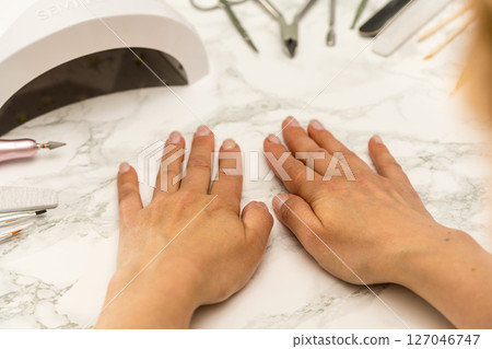 Nail manicure at home, female hands on the table with uv lamp and manicure tools Nail manicure at home, female hands on the table with uv lamp and manicure tools 127046747