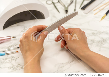 Gel nail manicure at home, female hands with nail file 127046749