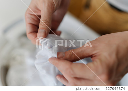 Close-up of male hands inspecting white garment for stains before putting in washing basin, demonstrating careful laundry process. Concept of domestic work, housekeeping and household. 127046874