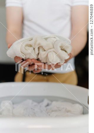 Vertical cropped shot of unrecognizable man soaking dirty white clothes in plastic basin, preparing for laundry with stain remover, close-up. Concept of domestic work, housekeeping and household. 127046889