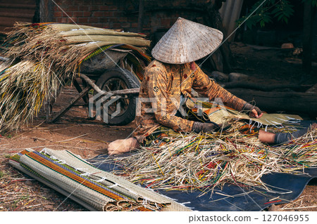 Vietnamese woman in straw hat works at a reed mat factory in Vietnam Vietnamese woman in straw hat works at a reed mat factory in Vietnam 127046955