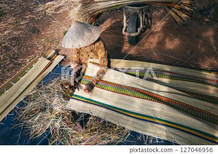 Vietnamese woman worker in traditional straw hat Non La works at a reed mat factory in craft village in Vietnam 127046956