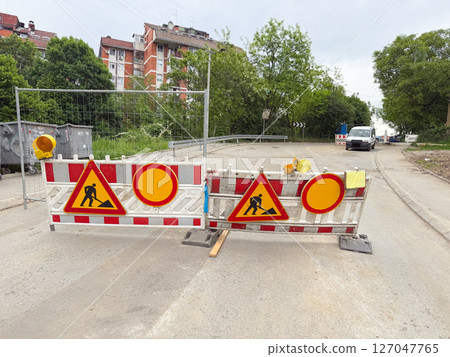 Street closed with multiple construction signs and warning barriers. Temporary roadblock signals active maintenance work. 127047765