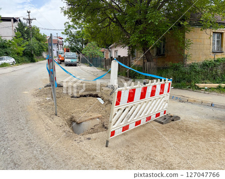 Open utility trench fenced off on a quiet suburban street. Safety barriers ensure protection during underground works. 127047766