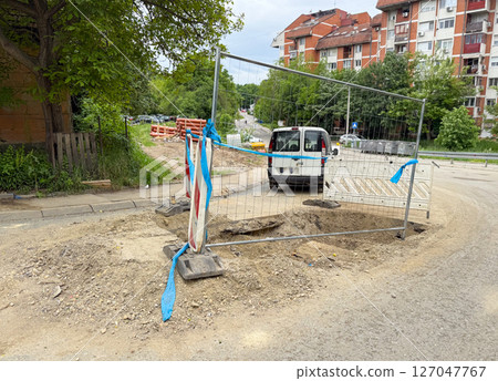 Roadside excavation area secured with barriers and a parked service van. Infrastructure maintenance in progress. 127047767