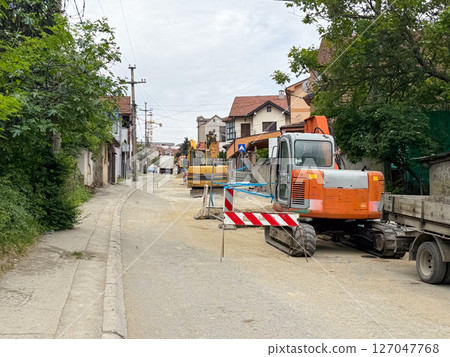Construction vehicles and barriers on quiet residential street under maintenance. Infrastructure upgrade in progress. 127047768