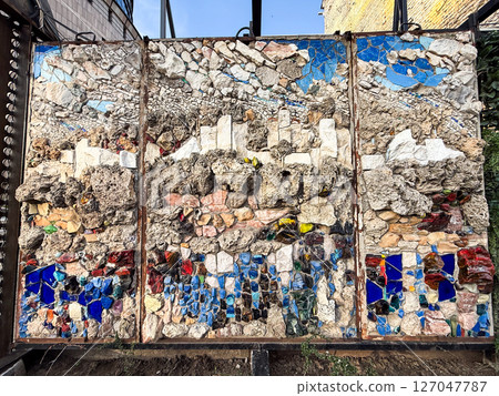 Mosaic wall with abstract cityscape crafted from natural stones and colored glass. Urban creativity and architectural detail Mosaic wall with abstract cityscape crafted from natural stones and colored glass. Urban creativity and architectural detail 127047787