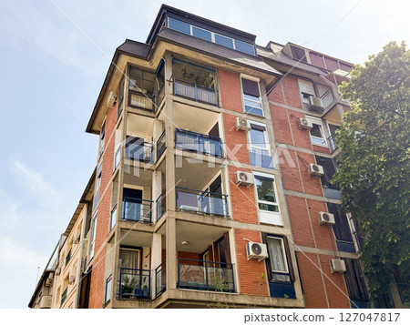 Residential building with balconies and red brick facade. Multi-story apartment structure featuring glass railings and air conditioning units. 127047817
