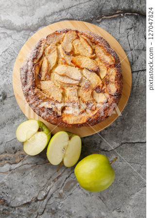 Apple Clafoutis is a delightful French-inspired dessert that combines tender, caramelized apples with a rich custard-like batter close-up. Vertical top view 127047824