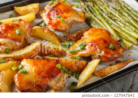 Baked chicken thighs in honey mustard sauce with potato wedges and asparagus close-up on a baking sheet. Horizontal Baked chicken thighs in honey mustard sauce with potato wedges and asparagus close-up on a baking sheet. Horizontal 127047841