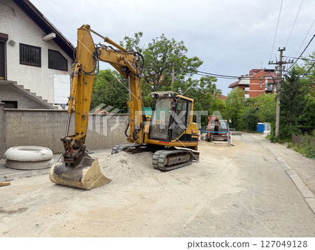 Excavator parked on a residential street during roadwork. Urban infrastructure repair in a suburban neighborhood. 127049128