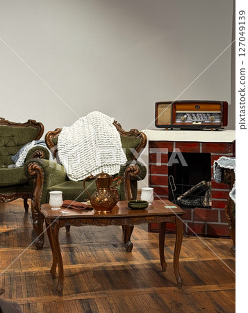 Cozy vintage living room with green armchairs and wooden coffee table. Warm atmosphere with retro fireplace and antique radio. 127049139