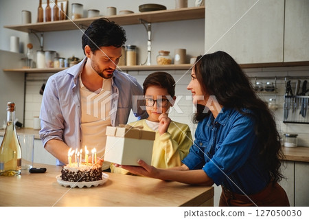 Family celebration with birthday cake and presents in a cozy kitchen Family celebration with birthday cake and presents in a cozy kitchen 127050030