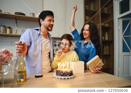 Family celebrates a childs birthday with cake and gifts at home 127050036