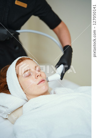 Woman receiving facial treatment in spa during daytime session 127050141
