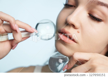 Elegant woman examining skin using magnifying glass in bright setting 127050151