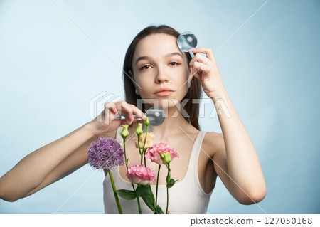 Woman holds flowers while using magnifying glasses for observation Woman holds flowers while using magnifying glasses for observation 127050168