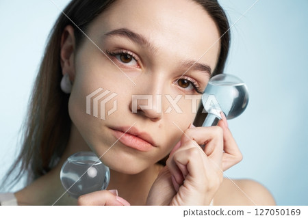Young woman engages in skincare routine with facial tools in bright setting 127050169