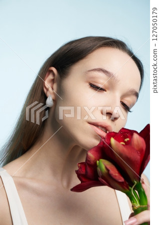 Young woman appreciating red flowers against a light blue background Young woman appreciating red flowers against a light blue background 127050179