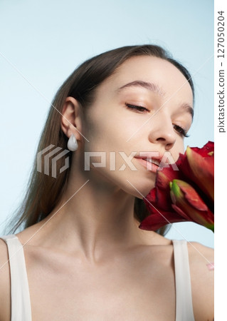 Woman holds red flower admiring fragrance with serene expression in studio Woman holds red flower admiring fragrance with serene expression in studio 127050204