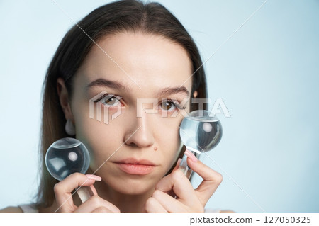 Woman using magnifying glasses for skin analysis in a studio setting Woman using magnifying glasses for skin analysis in a studio setting 127050325