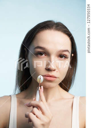 Young woman using facial roller for skincare routine Young woman using facial roller for skincare routine 127050334