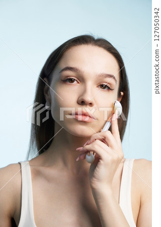 Woman using facial roller on her cheek for skincare routine indoors Woman using facial roller on her cheek for skincare routine indoors 127050342