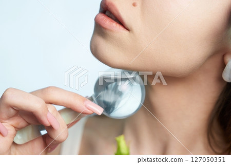 Woman using a magnifying glass for skin inspection near a plant 127050351