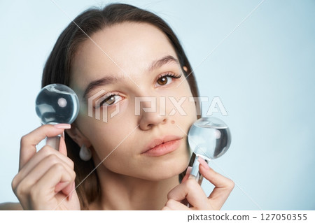Woman holding magnifying glasses while posing against light blue backdrop 127050355