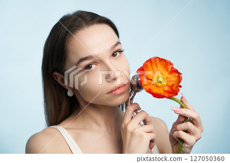 Woman holding a bright flower while applying skincare in bright studio Woman holding a bright flower while applying skincare in bright studio 127050360