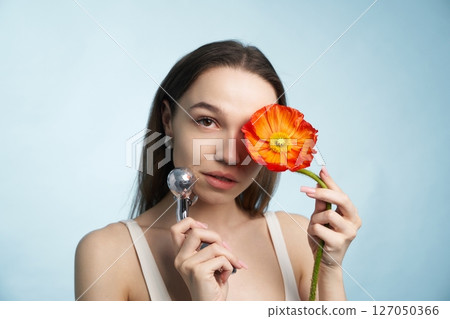 Young woman holds a flower and tool for beauty care in soft lighting Young woman holds a flower and tool for beauty care in soft lighting 127050366