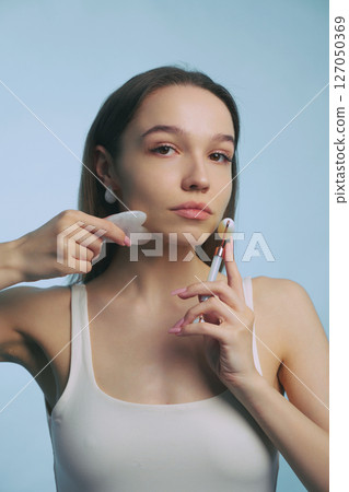 Woman applying makeup with sponge and brush against blue background 127050369