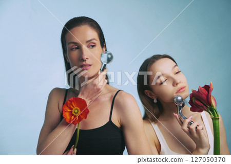 Two women enjoying skincare routine with facial tools and flowers 127050370