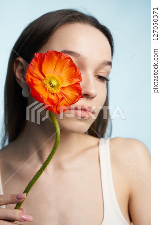 Woman holds vibrant orange flower close to her face in soft lighting 127050371