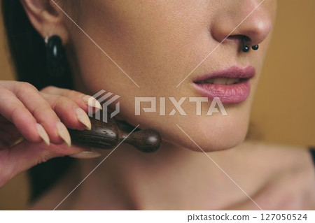 Woman using a wooden tool for facial massage at home in natural light 127050524