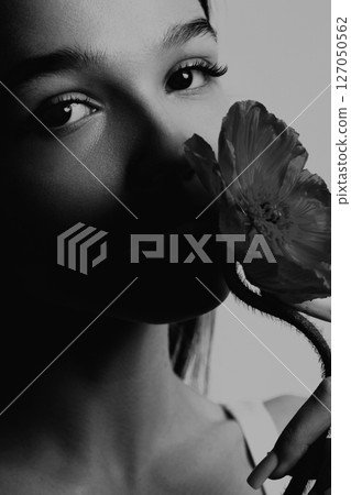 Young woman holding flower while partially in shadow against light background 127050562