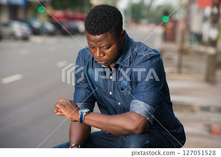 young man is watching the watch in his hand waiting for a late m young man is watching the watch in his hand waiting for a late m 127051528
