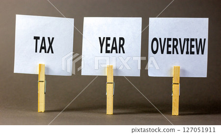 Tax year overview symbol. Concept words Tax year overview on beautiful white paper on clothespin. Beautiful grey background. Business tax year overview concept. Copy space. Tax year overview symbol. Concept words Tax year overview on beautiful white paper on clothespin. Beautiful grey background. Business tax year overview concept. Copy space. 127051911