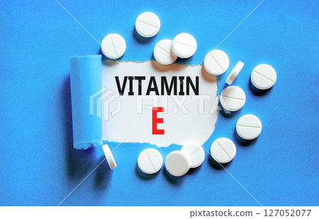 Vitamin E tocopherols symbol. Concept words Vitamin E on beautiful white paper. White pills tablets. Beautiful blue background. Medical healthy lifestyle Vitamin E tocopherols concept. 127052077