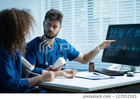 doctor checking woman blood pressure at clinic and filling patient history. doctor checking woman blood pressure at clinic and filling patient history. 127052583