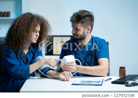 doctor checking woman blood pressure at clinic and filling patient history. 127052586