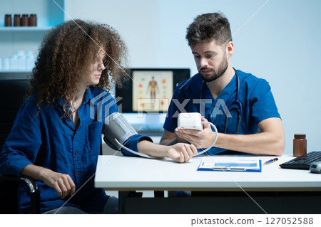 doctor checking woman blood pressure at clinic and filling patient history. 127052588