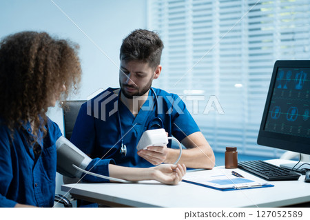 doctor checking woman blood pressure at clinic and filling patient history. doctor checking woman blood pressure at clinic and filling patient history. 127052589