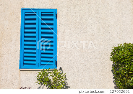 Blue shutter on beige wall. Mediterranean architecture, summer aesthetic, and coastal urban design with natural elements. Blue shutter on beige wall. Mediterranean architecture, summer aesthetic, and coastal urban design with natural elements. 127052691