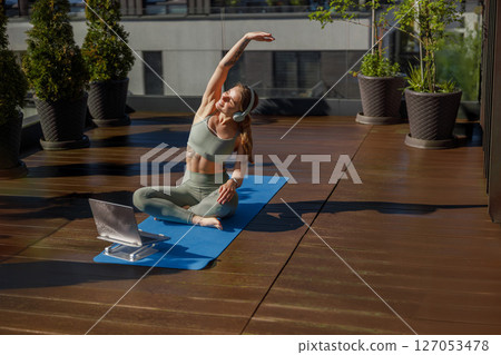 Engaging in a Yoga Session on the Rooftop Surrounded by a Laptop and Lush Green Plants 127053478