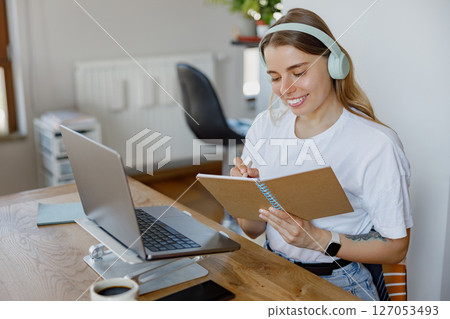 A Young Woman Engaged in Studying at Her Cozy Home with Both a Laptop and a Notebook Nearby A Young Woman Engaged in Studying at Her Cozy Home with Both a Laptop and a Notebook Nearby 127053493