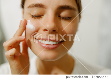 Skincare Routine Happy Woman Joyfully Applying Moisturizer in Her Bathroom Area Skincare Routine Happy Woman Joyfully Applying Moisturizer in Her Bathroom Area 127053548